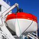 Lifeboat secured on a ship, orange top and white bottom, against a clear blue sky.