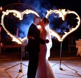 Ein Brautpaar küsst sich vor flammenden Herzen bei Nacht.