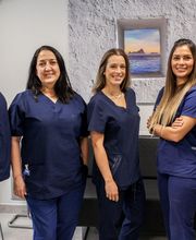 Cinco personas con uniformes médicos azules sonríen en una sala con un cuadro en la pared.