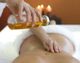 Person bei entspannender Massage mit warmem Öl, Kerzenlicht im Hintergrund.