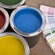Open paint cans of various colors next to paint swatches on a wooden surface.