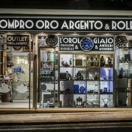 Facciata illuminata di un negozio di orologi e gioielli con insegne e vetrine espositive.