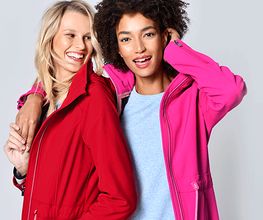 Zwei lächelnde Frauen in roten und pinken Jacken vor einem grauen Hintergrund.