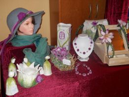 Hüte, Schmuck und Dekor auf rotem Tuch ausgestellt, mit Puppe und floralen Akzenten.