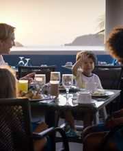 Familia cenando al aire libre frente al mar durante el atardecer.