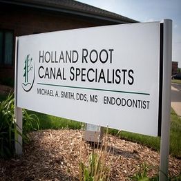 Sign for Holland Root Canal Specialists with greenery and a building in the background.