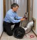 Man checking air duct with a testing device in a hallway.
