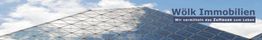 Glasgebäude mit Logo "Wölk Immobilien: Wir vermitteln das Zuhause zum Leben".