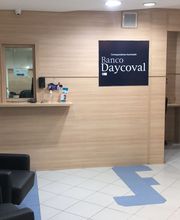 Recepção do Banco Daycoval com cadeiras pretas e materiais informativos em um balcão de madeira.