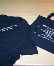 Schwarzes Hoodie und Tasche mit "Kosmetik Oase" Logo und Kontaktdetails auf Holzoberfläche.