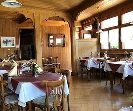 Gemütliches Restaurant mit Holzwänden, gedeckten Tischen und Blumen in einer sonnigen Atmosphäre.