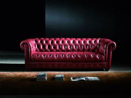Rotes Chesterfield-Sofa in dunklem Raum mit Teppich und Büchern im Vordergrund.