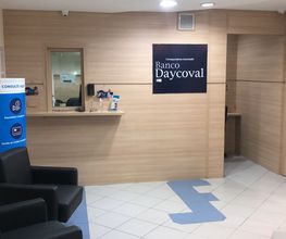 Recepção do Banco Daycoval com cadeiras pretas e materiais informativos em um balcão de madeira.
