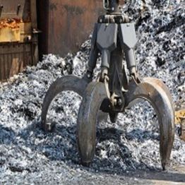 Ein Greifarm hebt Metallabfälle in einem Schrottplatzbereich auf, umgeben von Metallresten.