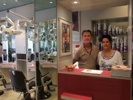 Ein Mann und eine Frau stehen lächelnd an einem Empfang in einem Friseursalon.