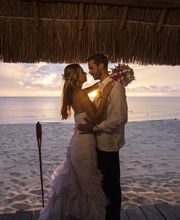 Pareja de recién casados se abraza en una playa al atardecer.