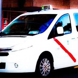 Taxi blanco con franja roja diagonal estacionado en la calle.