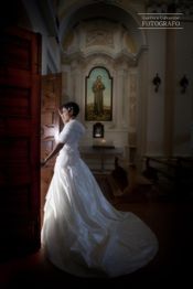 Sposa in abito bianco di fronte a una porta aperta in una chiesa.