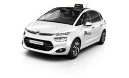 Taxi blanco Citroën C4 Picasso visto de frente con letrero de taxi en el techo.