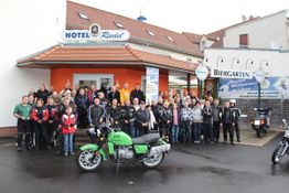 Gruppe von Menschen vor einem Hotel mit einem grünen Motorrad im Vordergrund.