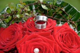 Rote Rosen mit Eheringen in einem silbernen Etui, dekoriert mit grünem Laub und weißen Perlen.