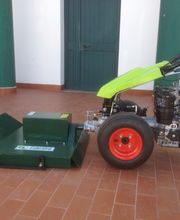 Motocoltivatore verde con falciatrice su pavimento di piastrelle rosse, davanti a una porta verde.