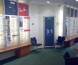 Opticienwinkel met brillen op displays en stoelen in een verlichte ruimte.