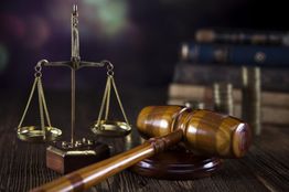 Weegschaal en hamer op houten tafel met boeken en munten op de achtergrond.