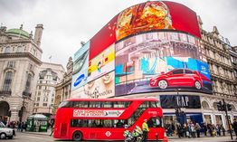 Roter Bus vor Werbetafeln am Piccadilly Circus in London, mit vielen Fußgängern im Hintergrund.