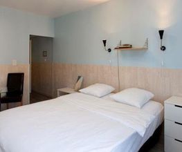 Helles Schlafzimmer mit Doppelbett, weißer Kommode, zwei Stühlen und einem kleinen Tisch.