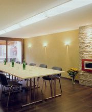 Moderner Konferenzraum mit langem Tisch, Stühlen, Steinfassade und großen Fenstern.