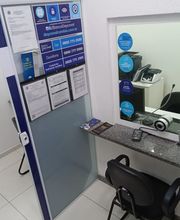 Sala de atendimento com parede de avisos, balcão com cadeira e equipamentos eletrônicos.