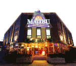 Außenansicht eines beleuchteten Gebäudes mit "Malibu" Schild und Palme darüber.