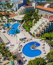 Vista aérea de un complejo hotelero con piscinas y palmeras junto a la playa.