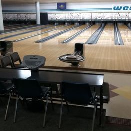 Empty bowling alley with four lanes, chairs, and ball returns visible.