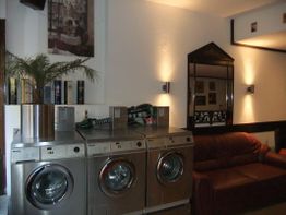 Waschsalon mit drei Waschmaschinen, einem braunen Sofa und Wanddekoration, gemütlich beleuchtet.