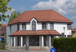 Zweistöckiges Gebäude mit rotem Dach, weißer Fassade und moderner Architektur bei Sonnenschein.