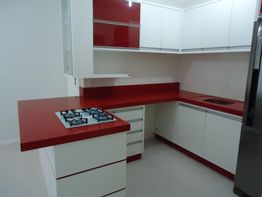 Cozinha moderna em L, com armários brancos e bancada vermelha, fogão embutido à esquerda.