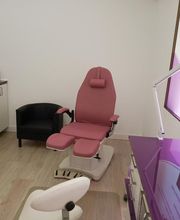 Sala de estética con silla reclinable rosa, muebles y lámpara, tonos morados y blancos.