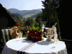 Tisch im Freien mit Blumen, Sektkühler und Hüten vor Berglandschaft bei sonnigem Wetter.