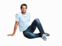 Ein lächelnder Mann sitzt entspannt im Schneidersitz auf dem Boden, trägt T-Shirt und Jeans.