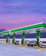Estación de servicio BP al atardecer con montañas al fondo y autos en las bombas de gasolina.