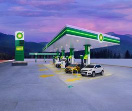 Estación de servicio BP al atardecer, con varios coches repostando y montañas al fondo.