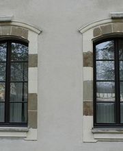 Zwei nebeneinanderliegende Fenster mit braunen Rahmen und gemustertem Mauerwerk.