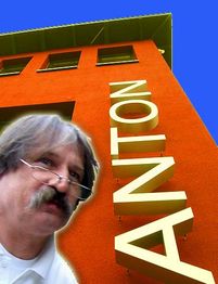 Mann mit Brille vor einem orangefarbenen Gebäude mit dem Schriftzug "ANTON" an der Fassade.