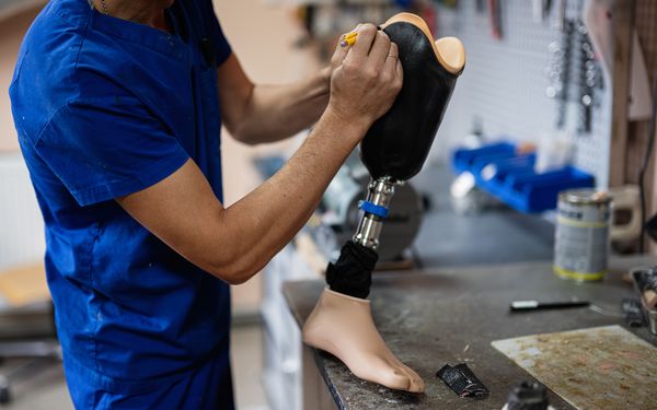 Mann in blauer Arbeitsuniform zeichnet an einer Prothese die genauen Maße an, um sie an den Kunden anzupassen.