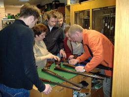 Menschen inspizieren Gewehre in einem Laden, stehen an einem Tresen und begutachten die Waffen.