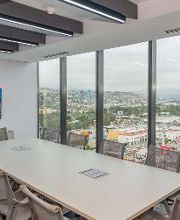Sala de reuniones con vista panorámica a la ciudad y televisión en pared.