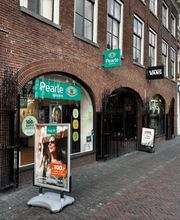 Winkelstraat met Pearle opticien en andere winkels, voetgangers op trottoir, bewolkte lucht.