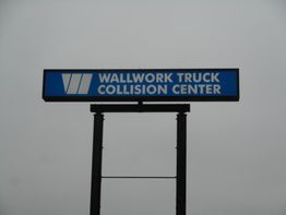 Sign reading "Wallwork Truck Collision Center" against a cloudy sky.